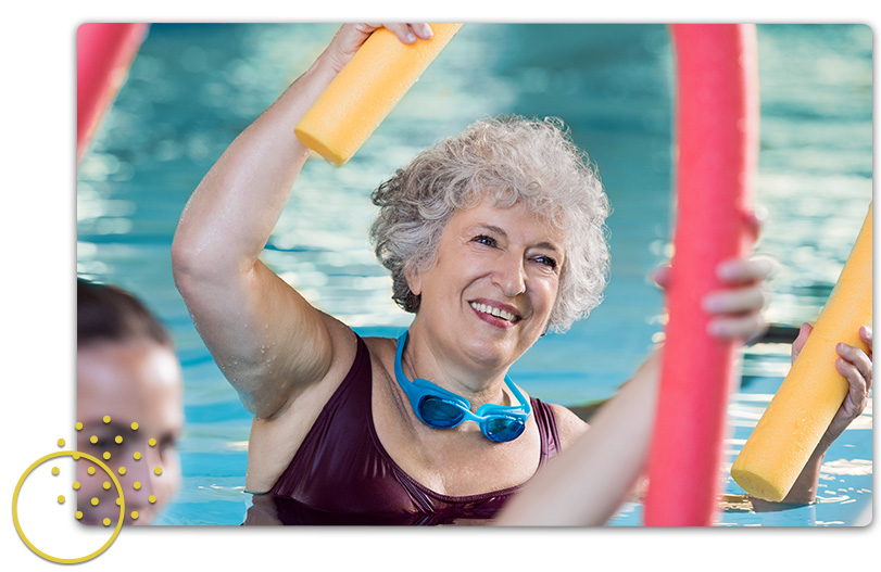 Smiling senior woman in maroon swimsuit doing pool exercises