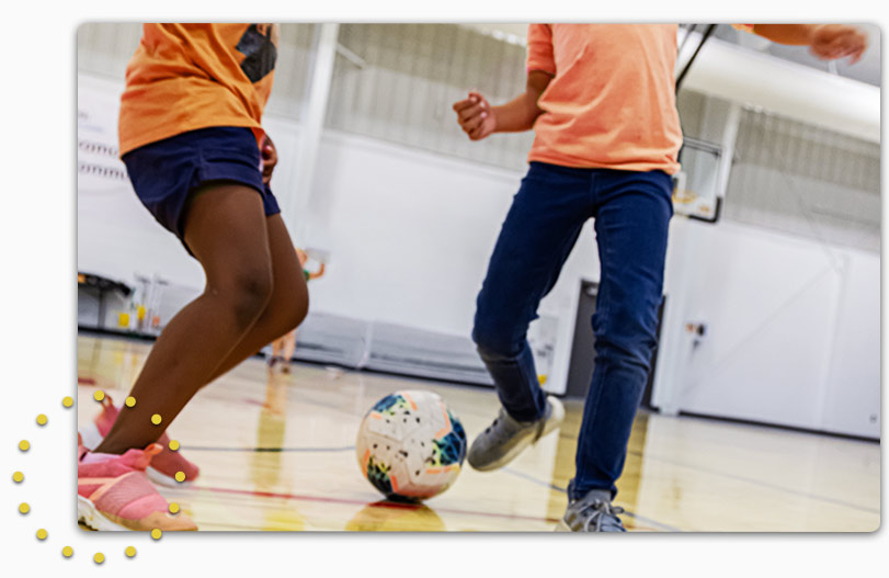 Boy and girl dribbling a soccer ball in gym